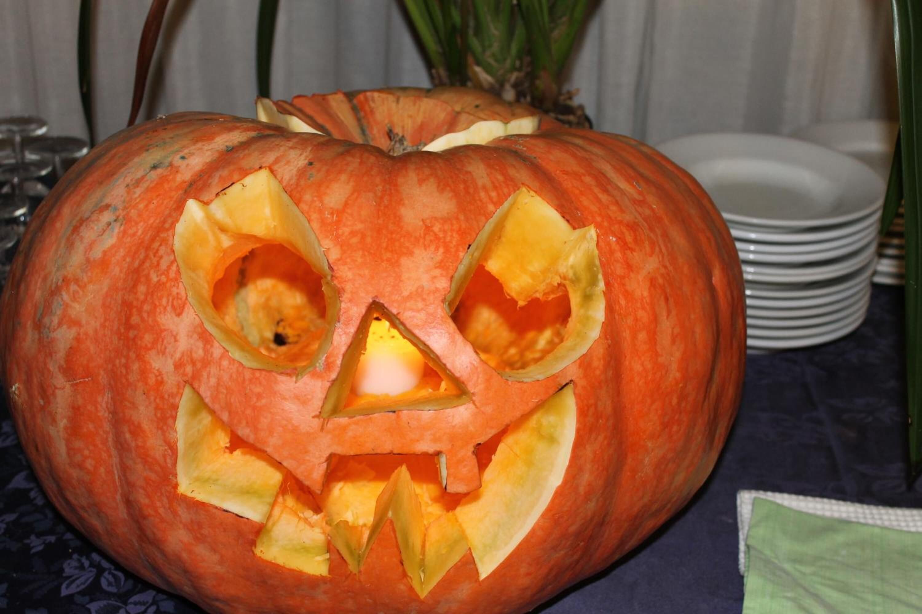 A carved pumpkin with a face, placed on a table with plates and a napkin.