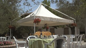 An outdoor dining area with a table covered by a green tablecloth, white plastic chairs, and a white canopy tent. - Hotel Ismaele (Chiusi)
