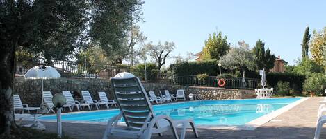 A pool area with white lounge chairs, a stone wall, and a clear blue sky.