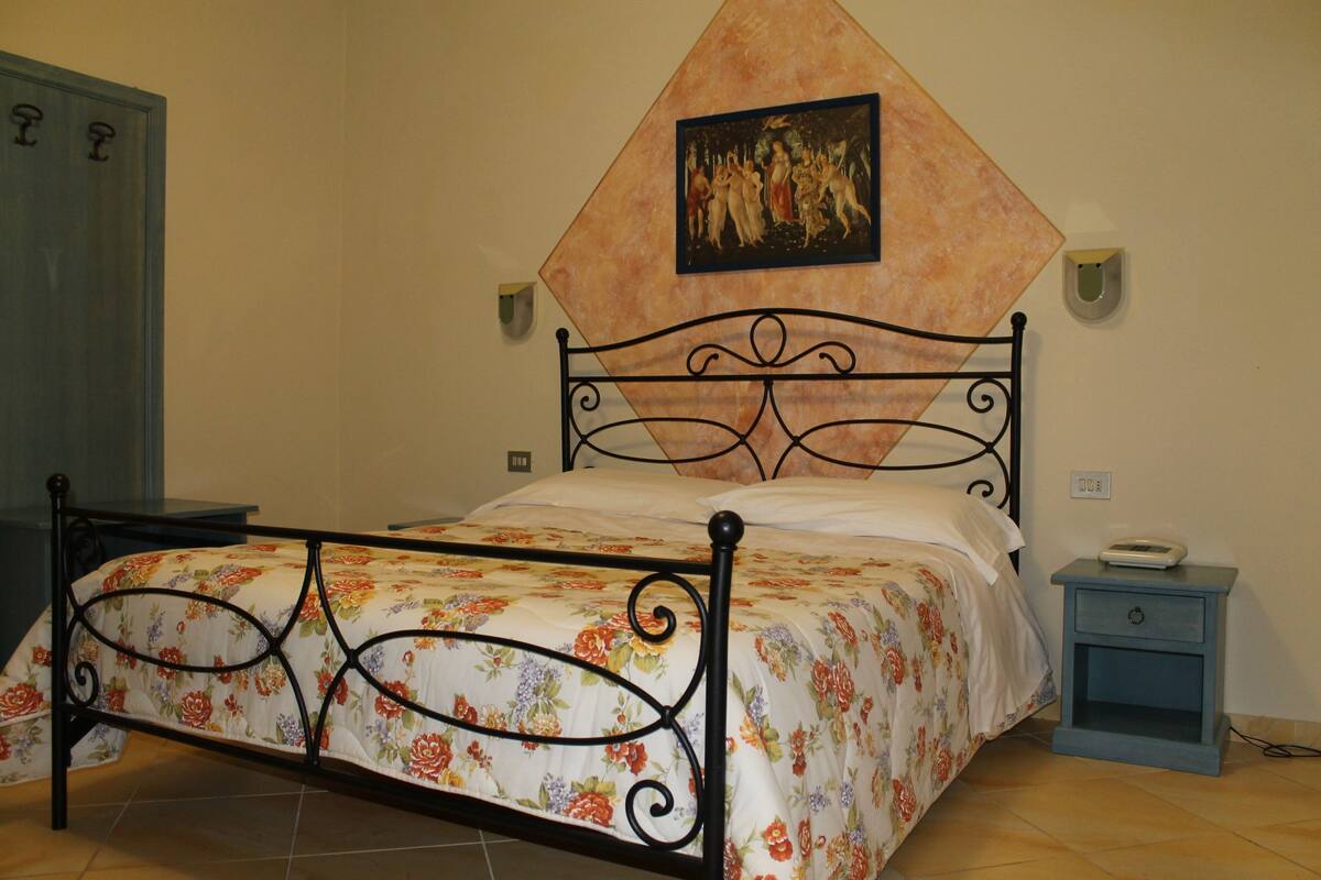 A bedroom with a bed, a nightstand, a wall-mounted picture, and a door.
