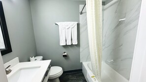 A bathroom with a toilet, sink, mirror, towel rack, shower curtain, and marble walls. - Catalina Airport Motel (Indianapolis)