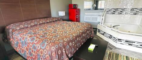 A hotel room with a bed, a red minibar, a white bathtub, and a striped rug.