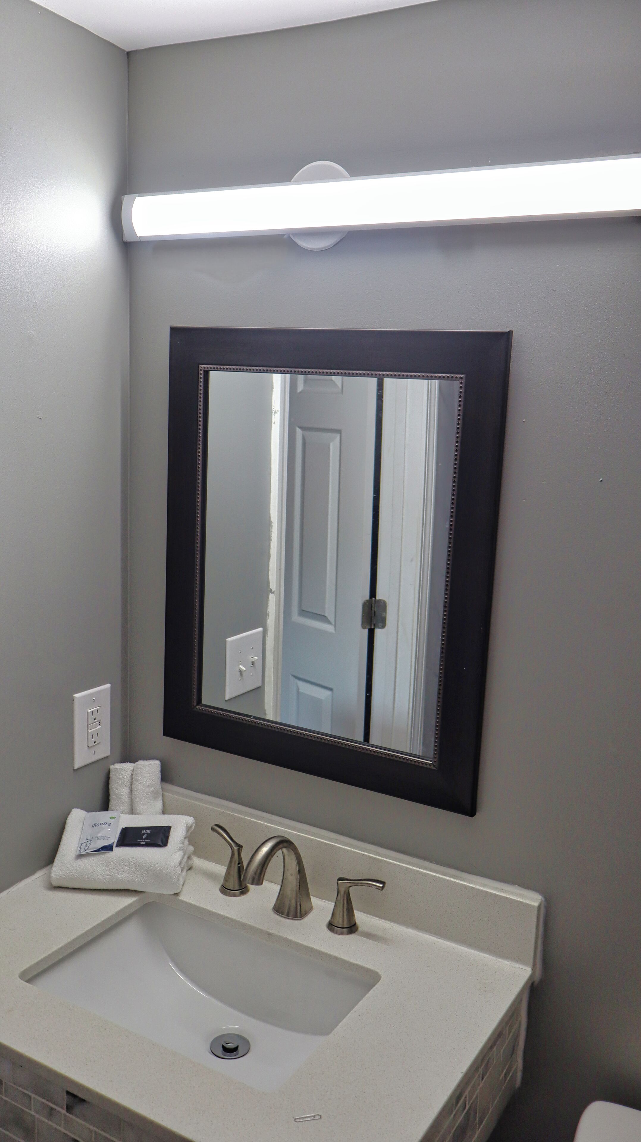 A bathroom with a sink, two faucets, a mirror, and a light above the mirror.