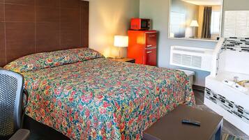 A hotel room with a bed, a small table, a sofa, a microwave, a cabinet, a mirror, and a bathtub.