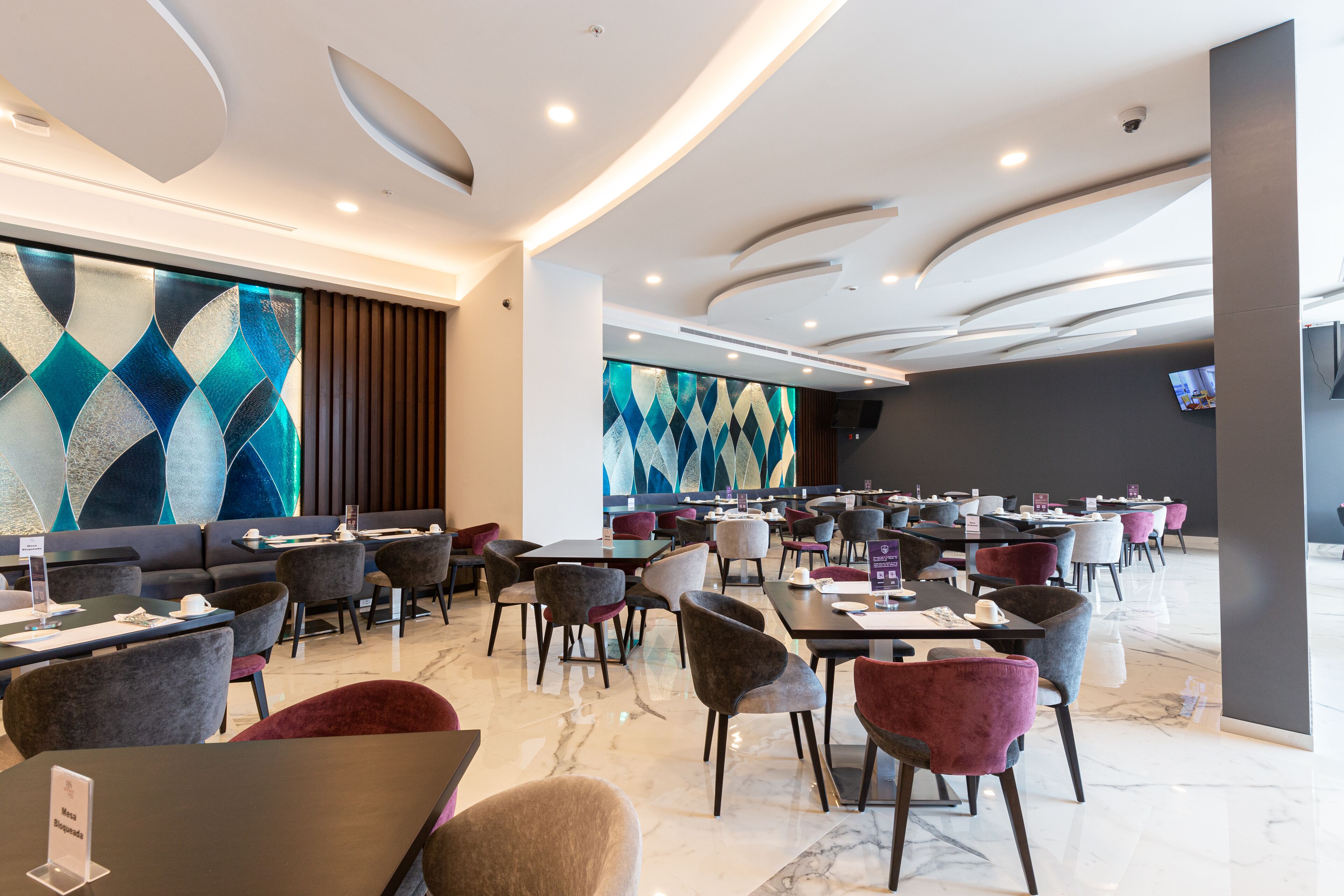Un restaurant moderne offrant différents types de sièges, notamment des tables et des chaises, ainsi qu’un grand mur décoratif orné de motifs géométriques.