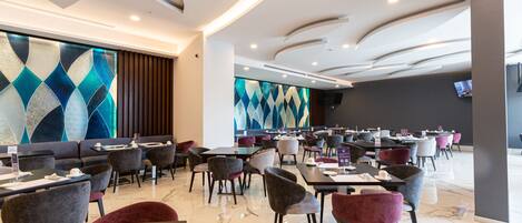 Un restaurante moderno con diversas opciones de asientos, como mesas y sillas, y una amplia pared decorativa con diseños geométricos.