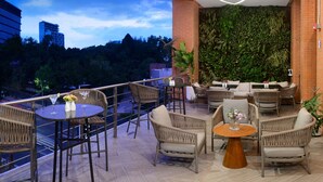 Un espace extérieur aménagé avec des meubles en osier, une table ronde et une vue sur le paysage urbain.