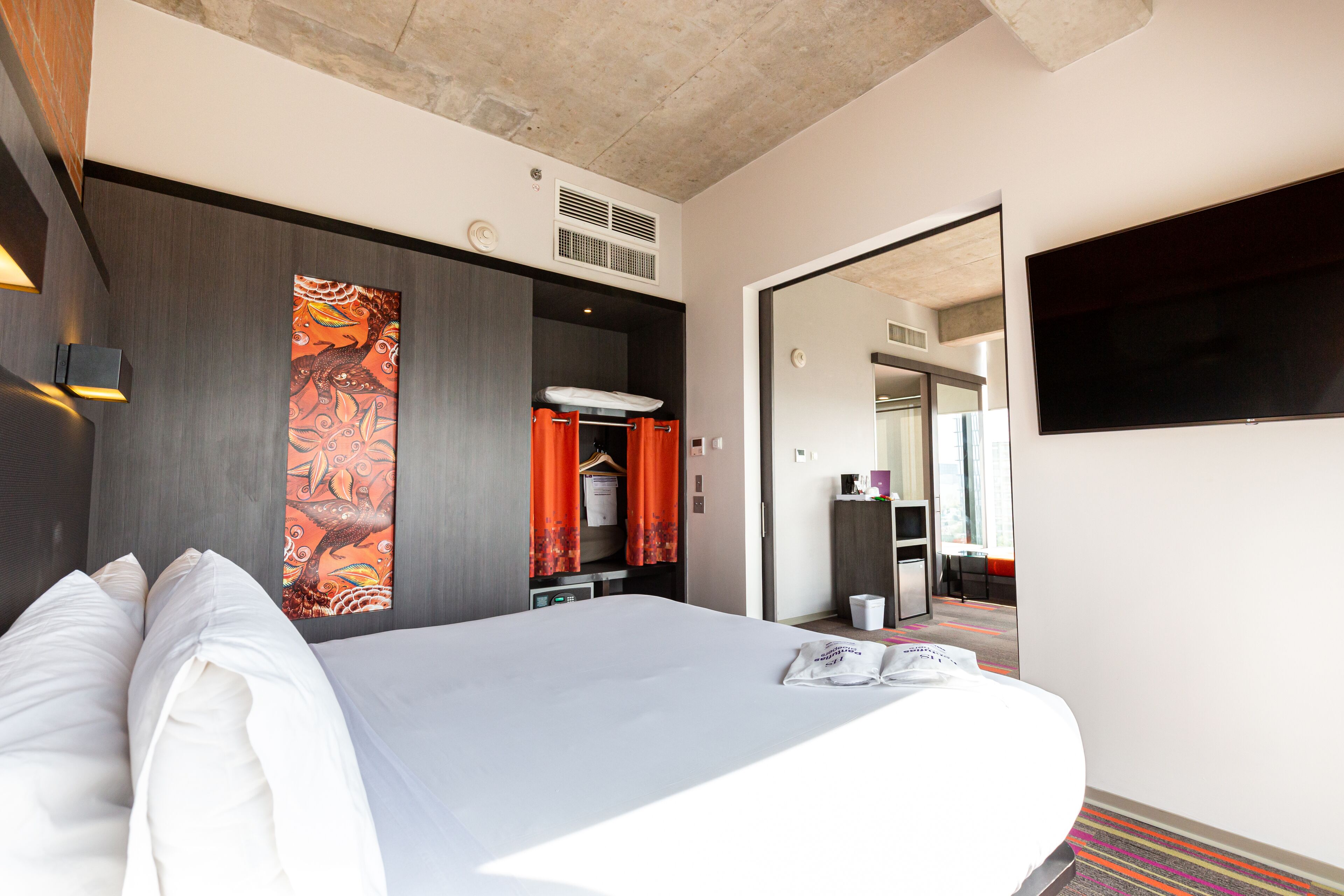 Una habitación de hotel con una cama grande, un armario, un espejo y un televisor.