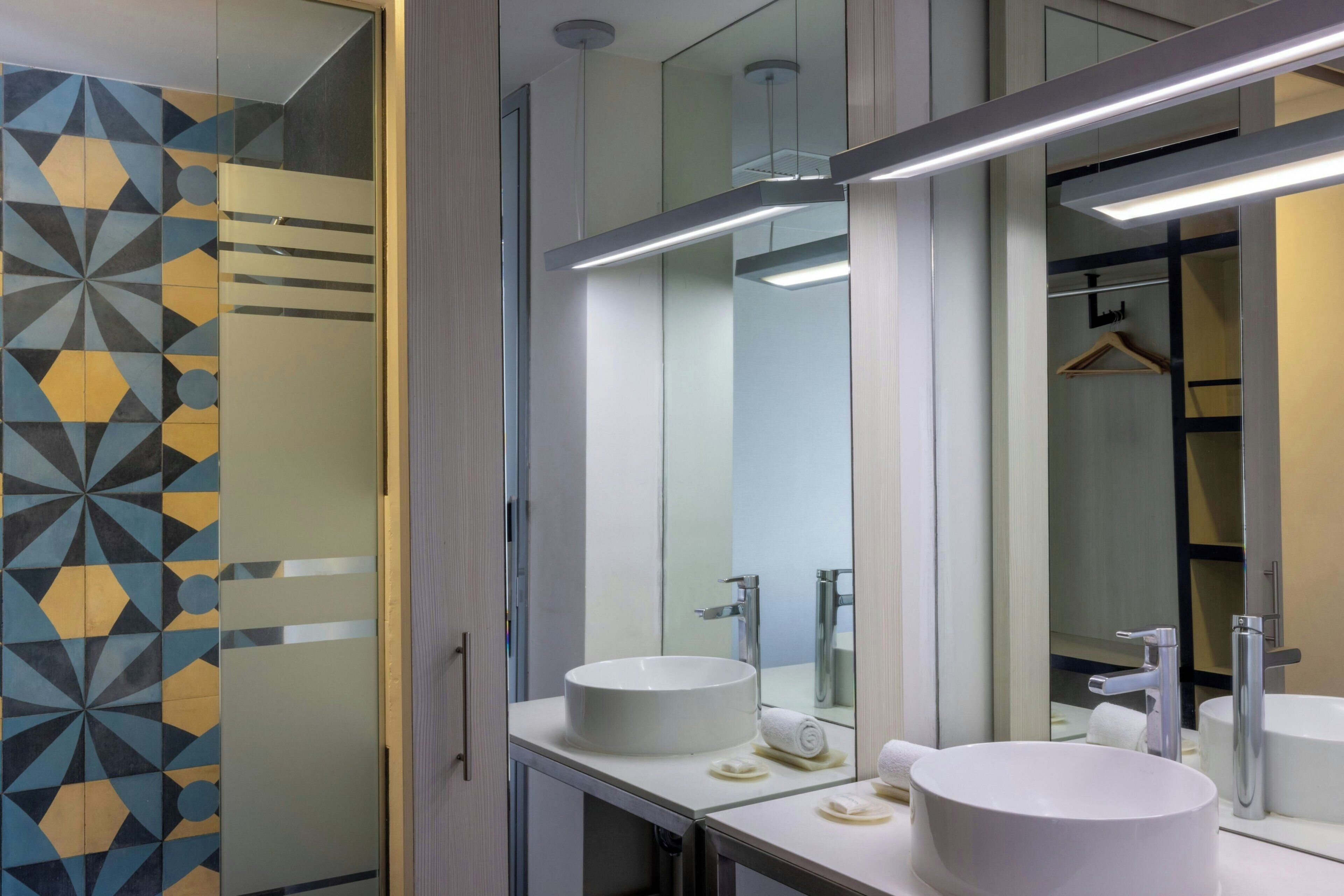 A modern bathroom with two sinks, a large mirror, and a geometric tile pattern on the wall.