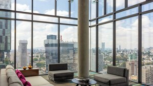 A modern living room with a large window, a sofa, two armchairs, and a coffee table. - Hotel Guadalajara Country Club by HNF (Guadalajara)