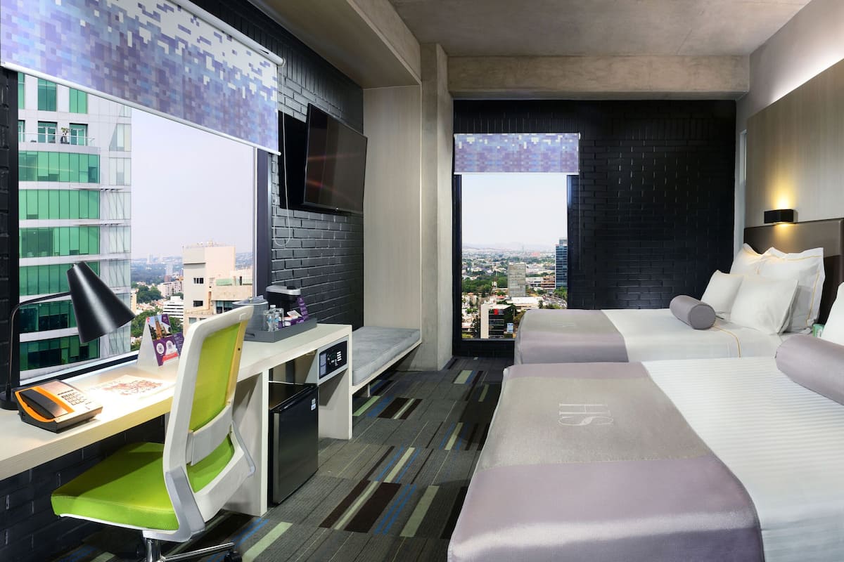 Habitación de hotel moderna con escritorio, dos camas, vistas de la ciudad y un ventanal grande.
