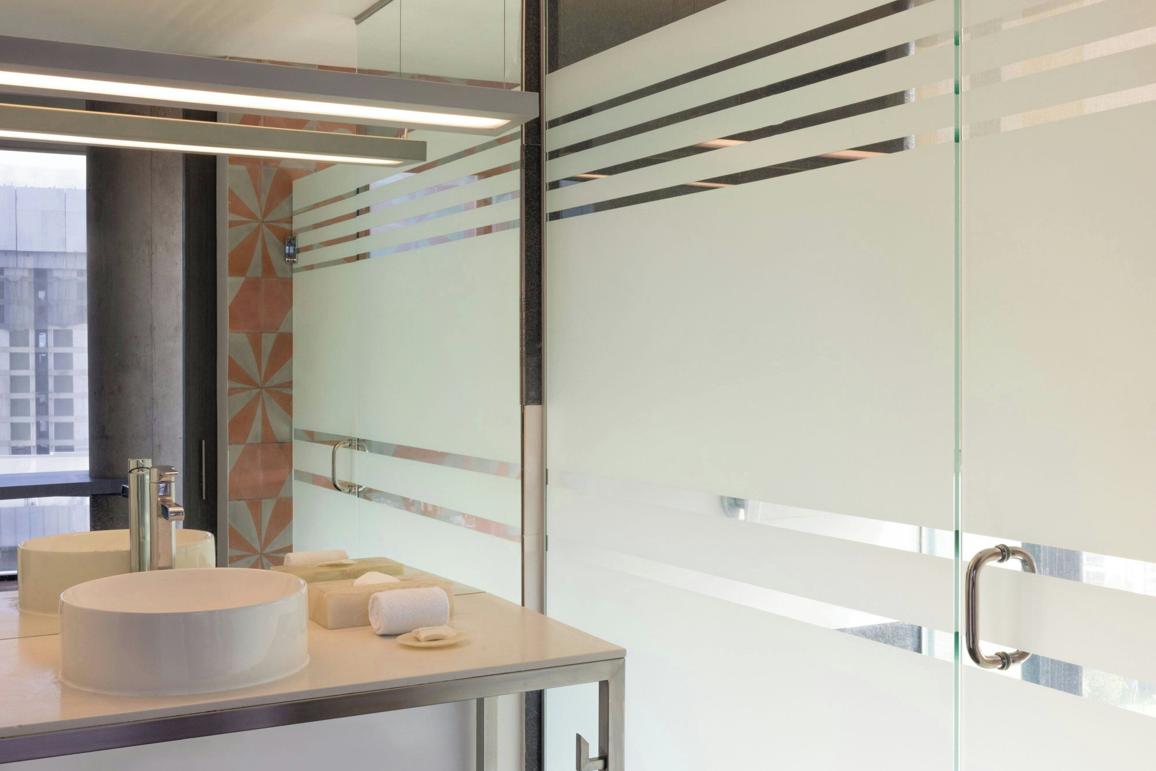 A modern bathroom with a large mirror, two sinks, and a glass partition.