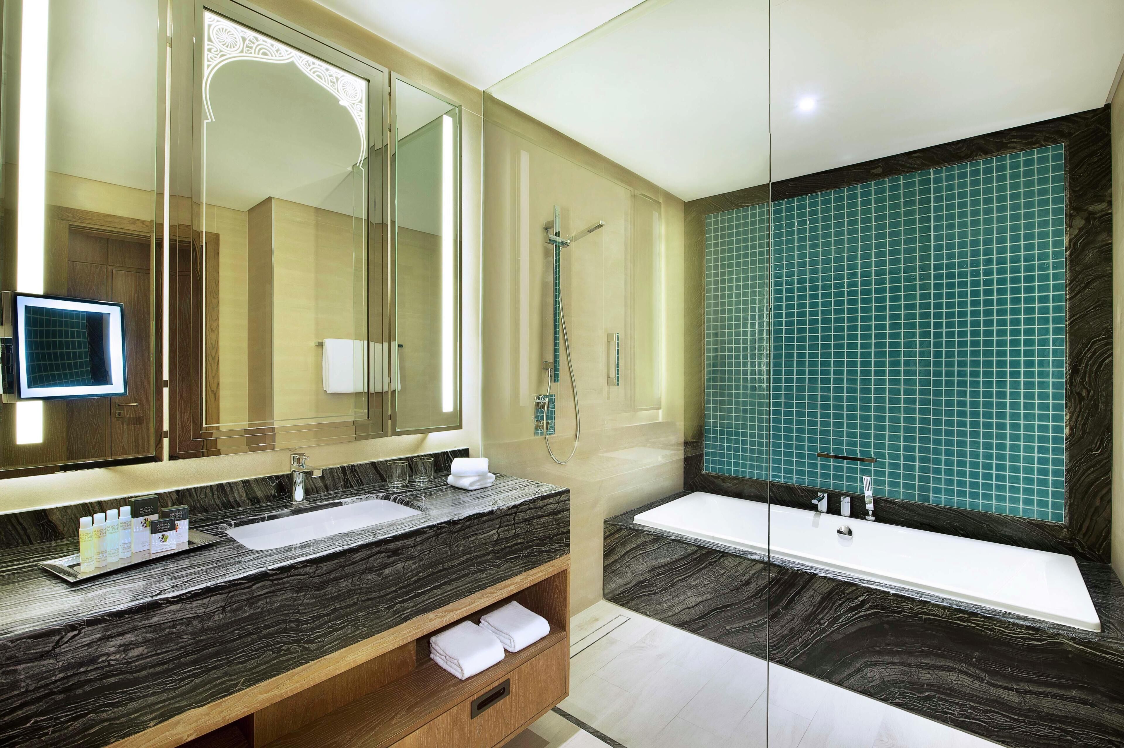 A modern bathroom with a large mirror, two sinks, a bathtub, and a shower.