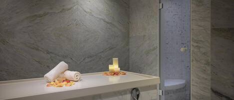 A bathroom with a marble wall, a white countertop, a towel, a soap bar, and a glass shower enclosure.
