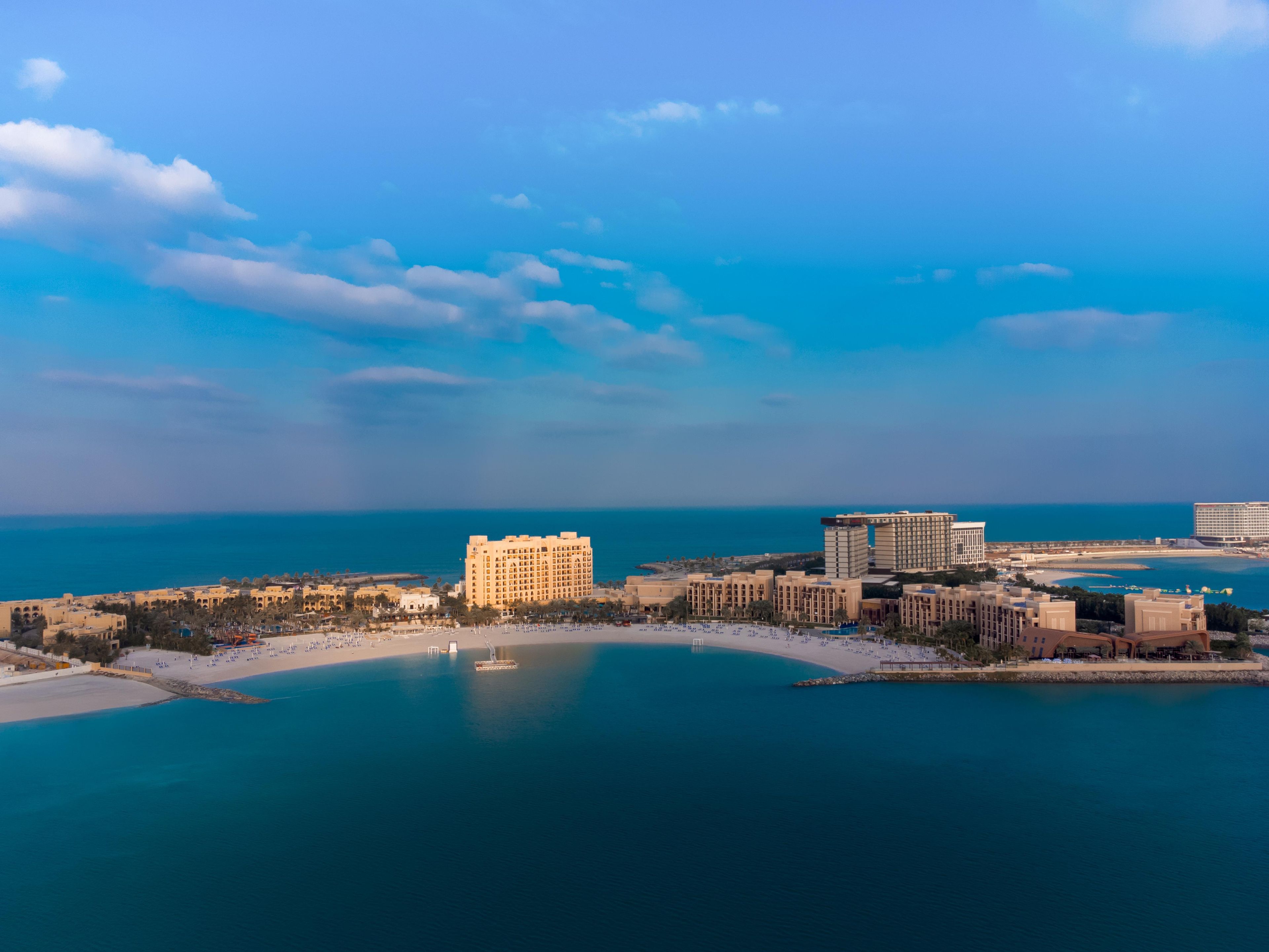 An aerial view of a coastal resort with multiple hotels, a beach, and clear blue waters.