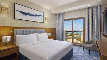 A hotel room with a large bed, a desk, a chair, a TV, and a balcony with a view.