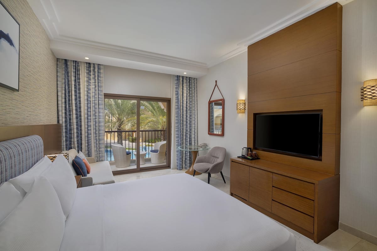 A hotel room with a large bed, a TV, a glass table, and a chair.