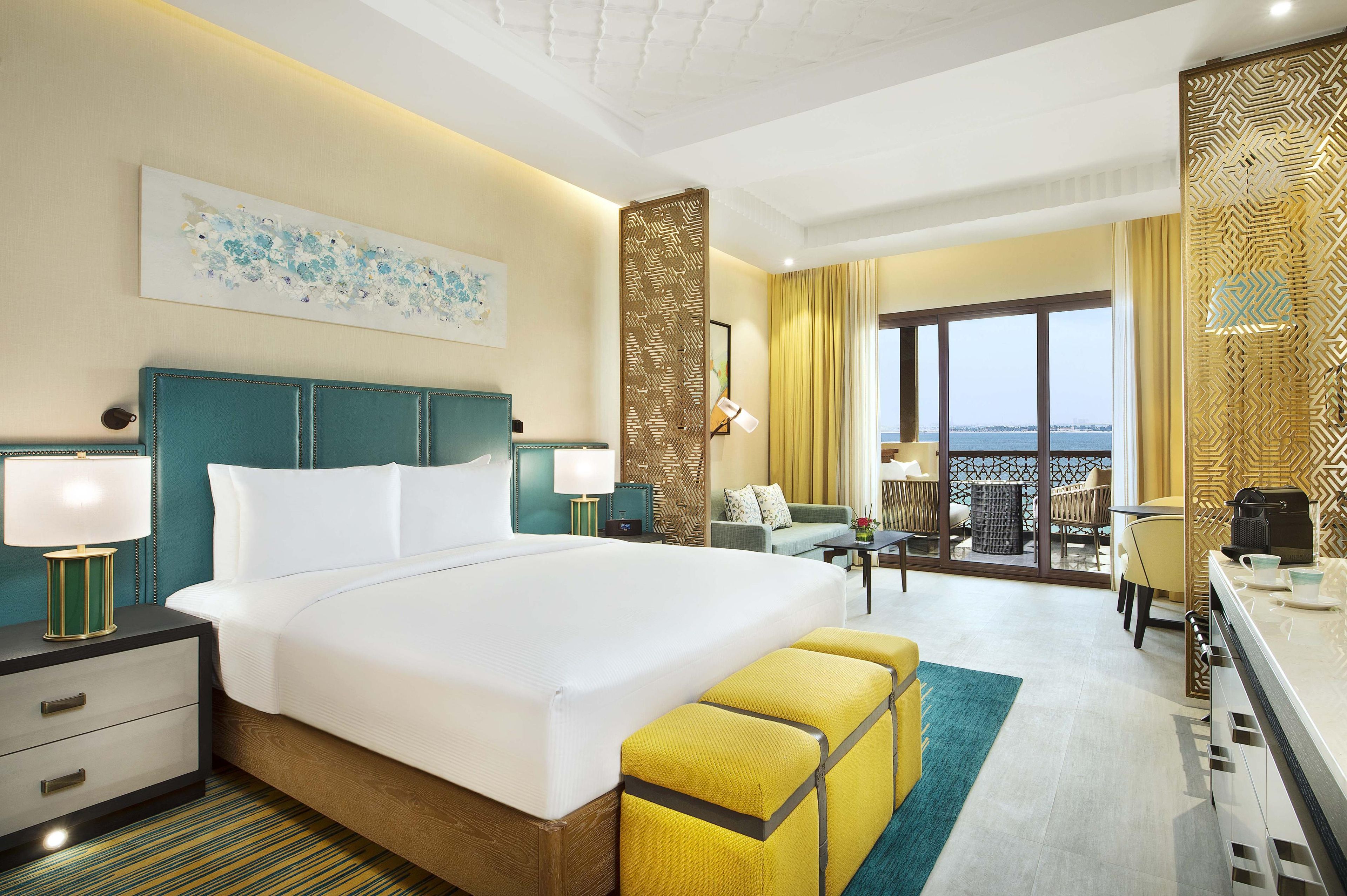 A hotel room with a large bed, a desk, a chair, a balcony with a view, and a decorative wall.