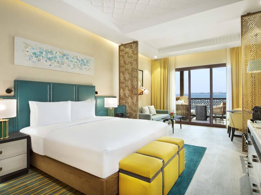 A hotel room with a large bed, a desk, a chair, a balcony with a view, and a decorative wall.
