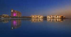 A waterfront hotel with a reflection in the calm water, featuring modern architecture and illuminated buildings. - DoubleTree by Hilton Resort & Spa Marjan Island (Ras Al Khaimah)