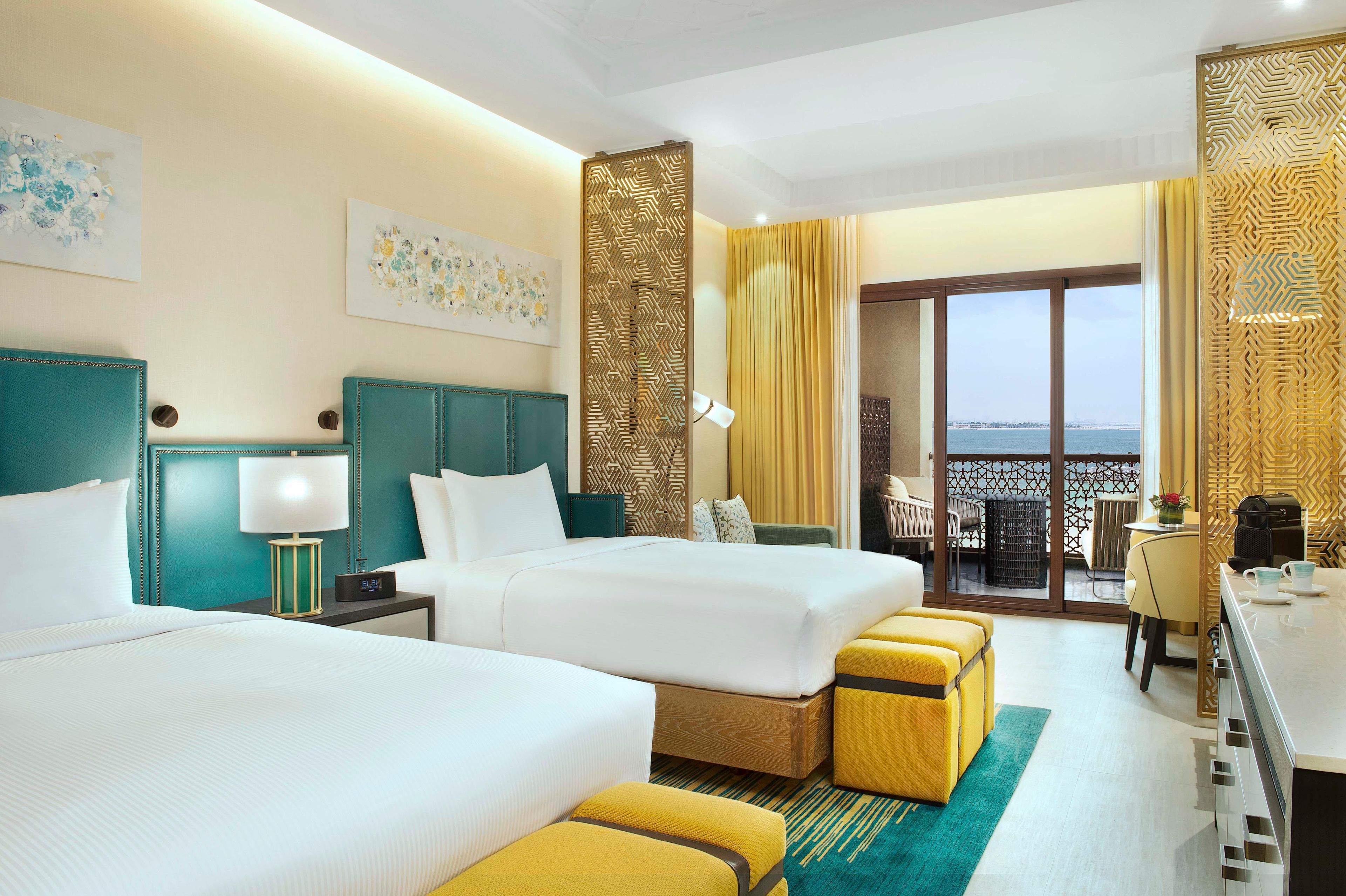 Habitación de hotel con dos camas, zona de comedor y balcón con vistas.