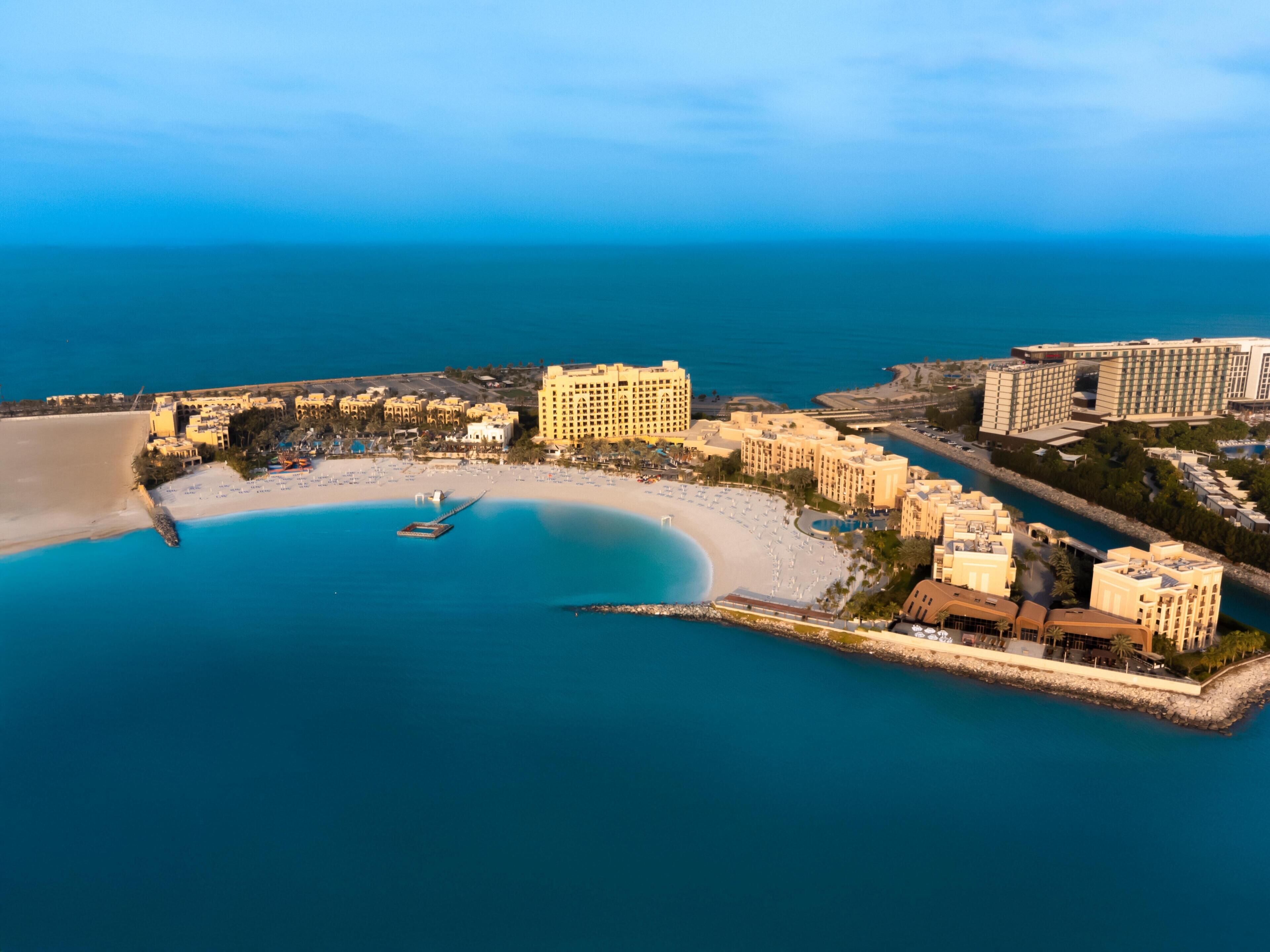 An aerial view of a coastal resort with beachfront villas, a marina, and a sandy beach.