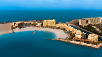 An aerial view of a coastal resort with beachfront villas, a marina, and a sandy beach.