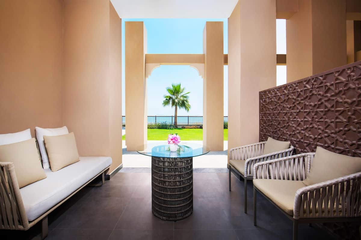 A room with a sofa, chairs, a glass-top table, and a view of a palm tree.