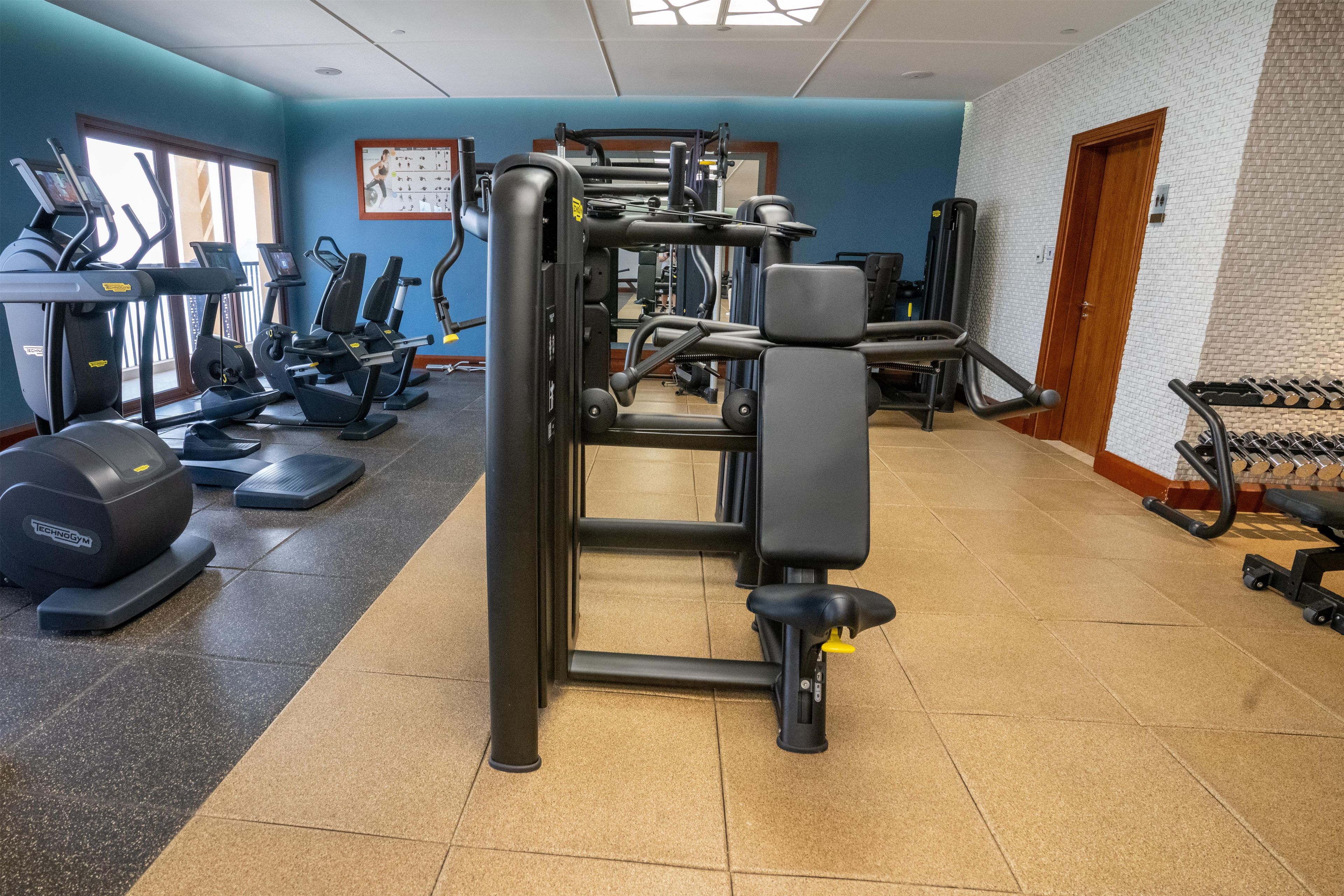 Ein Fitnessstudio mit verschiedenen Trainingsgeräten, darunter Laufbänder, Crosstrainer und Kraftgeräte.