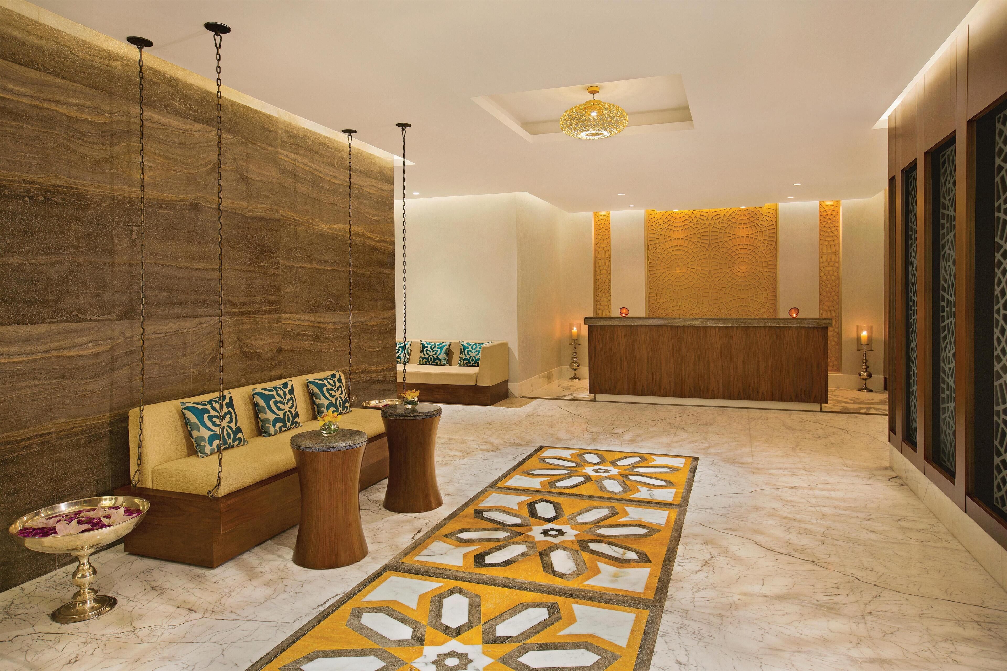 A lobby with a marble floor, a reception desk, a sofa with patterned cushions, and a hanging light fixture.