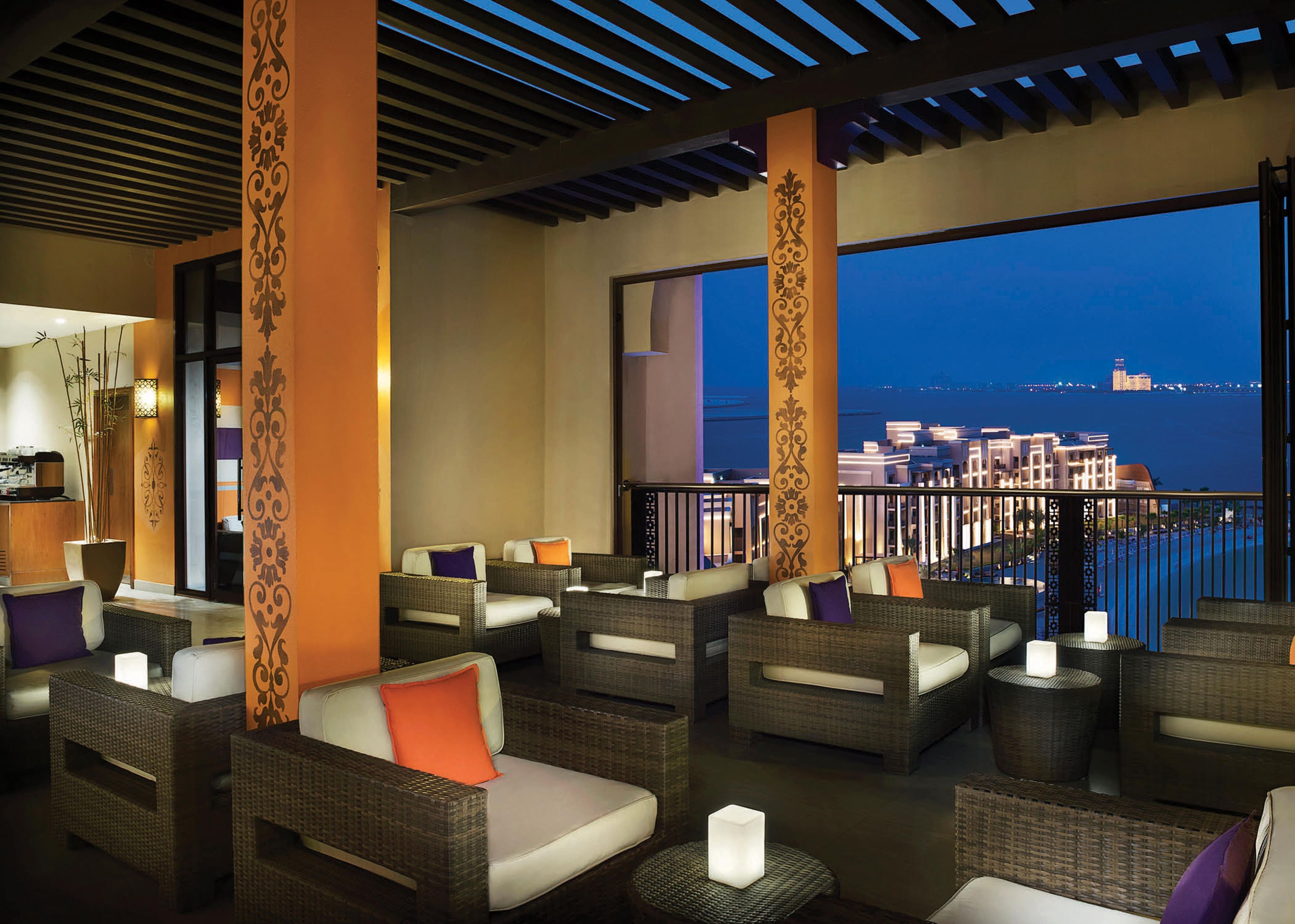 A balcony with wicker furniture and a city view at dusk.