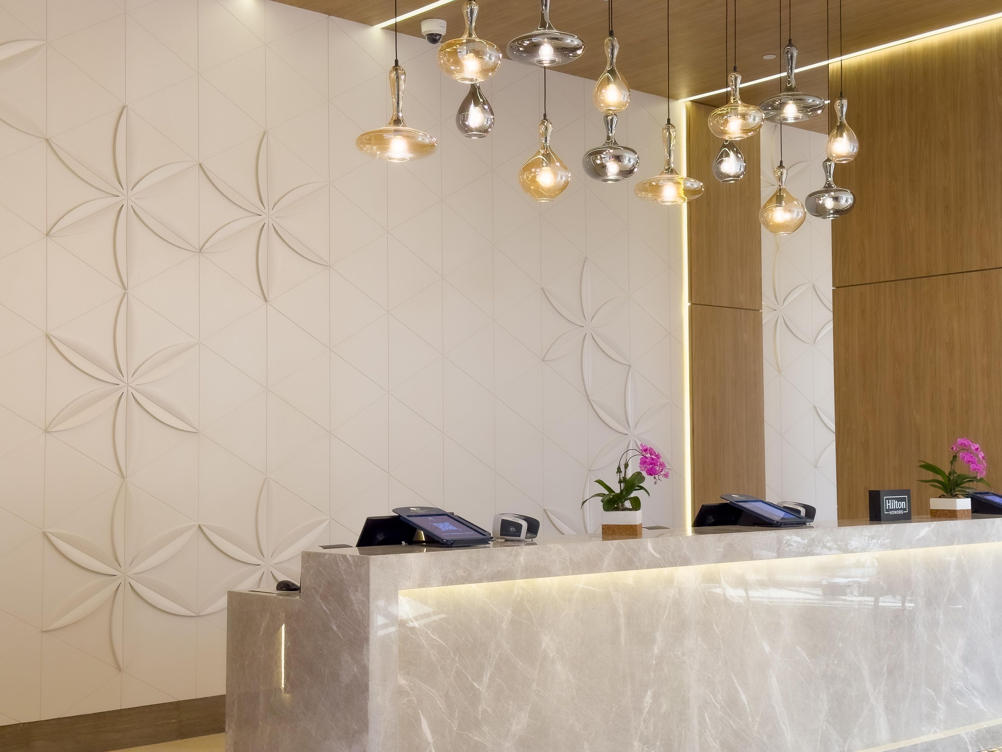 Ein Hotel-Empfangsbereich mit einer Marmor-Theke, Pendelleuchten und einer Wandgestaltung mit floralen Elementen.