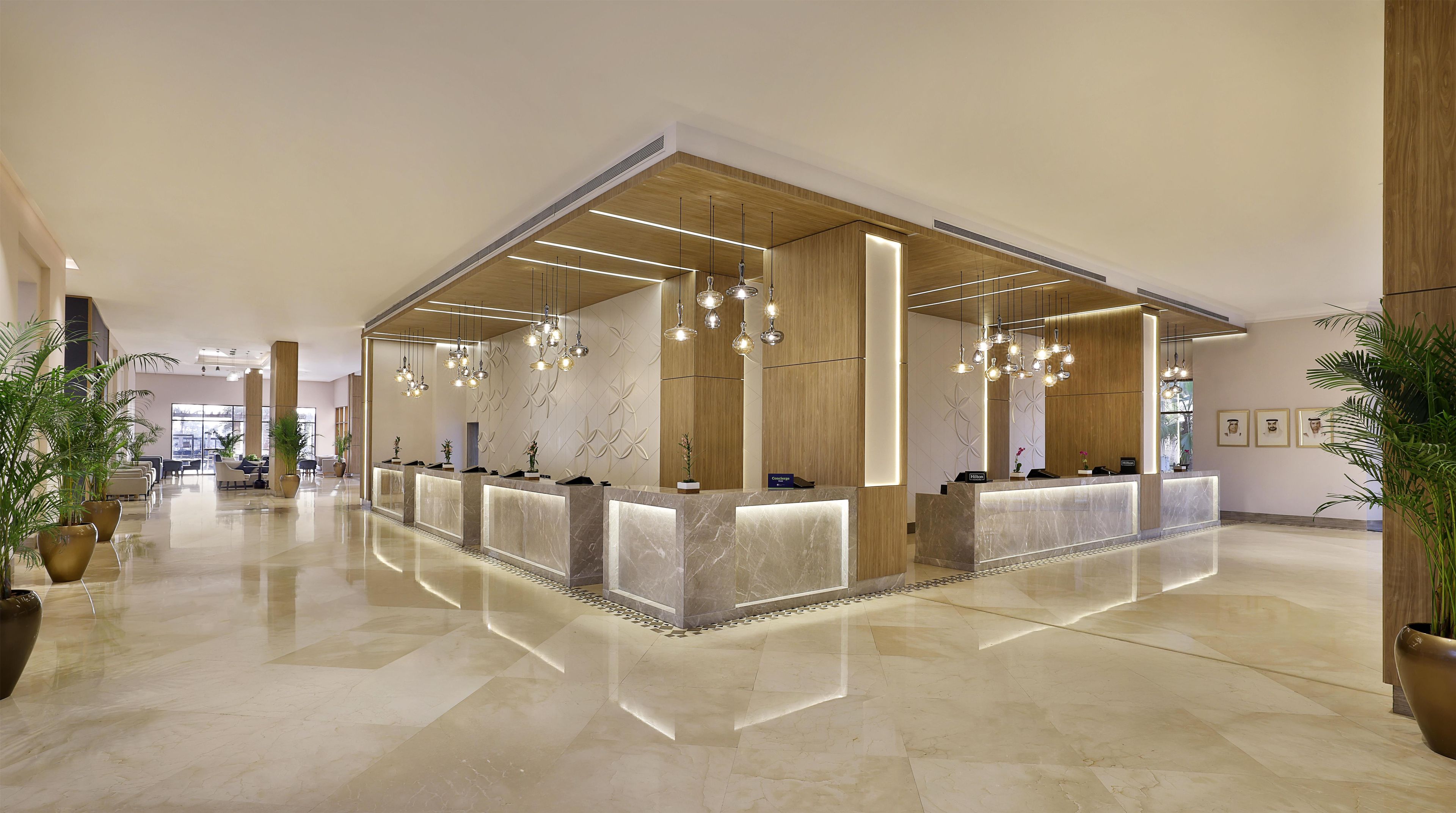 A modern hotel reception area with marble counters, pendant lighting, and potted plants.
