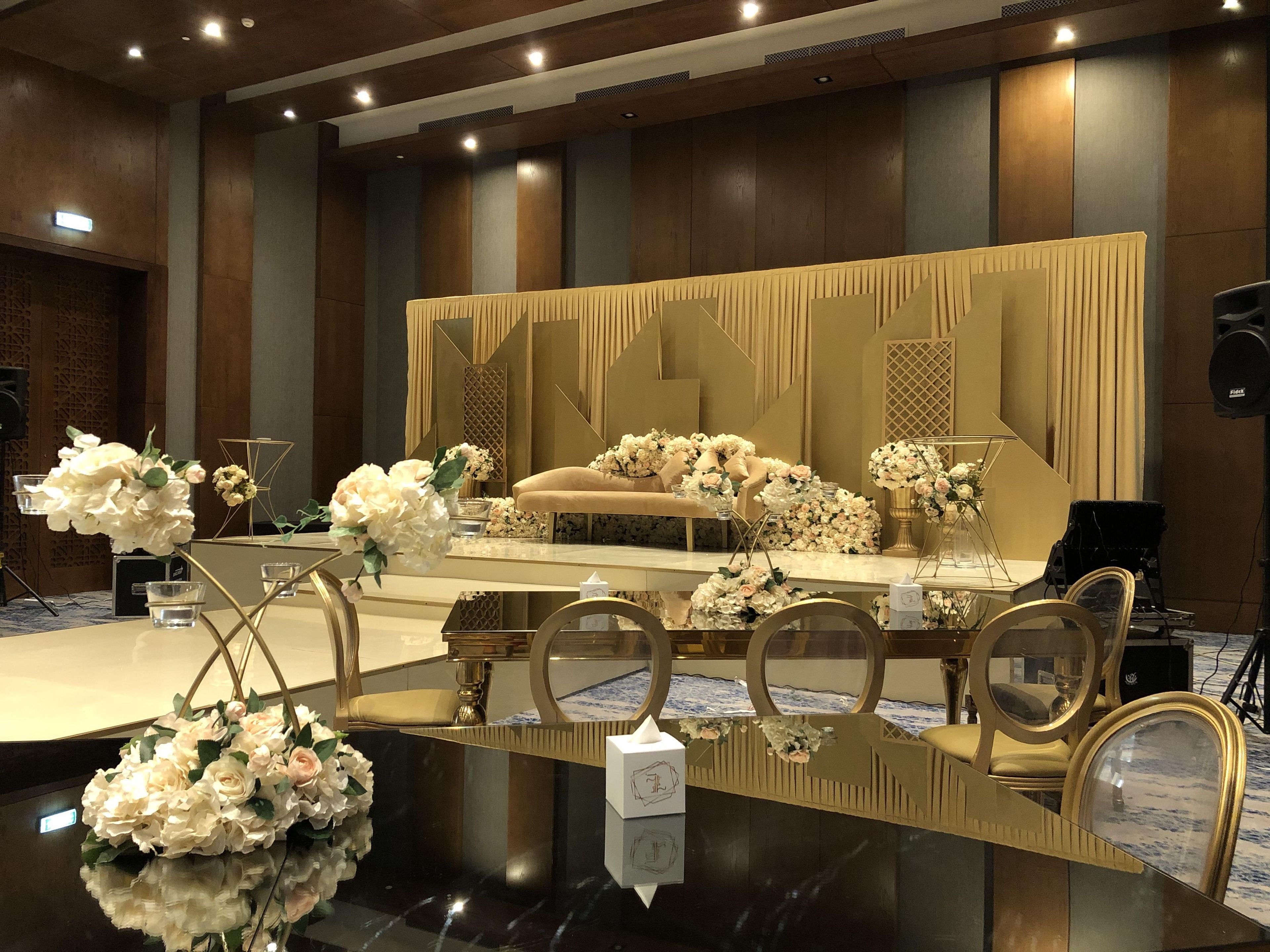 A stage with a golden backdrop, floral arrangements, and a seating area with chairs.
