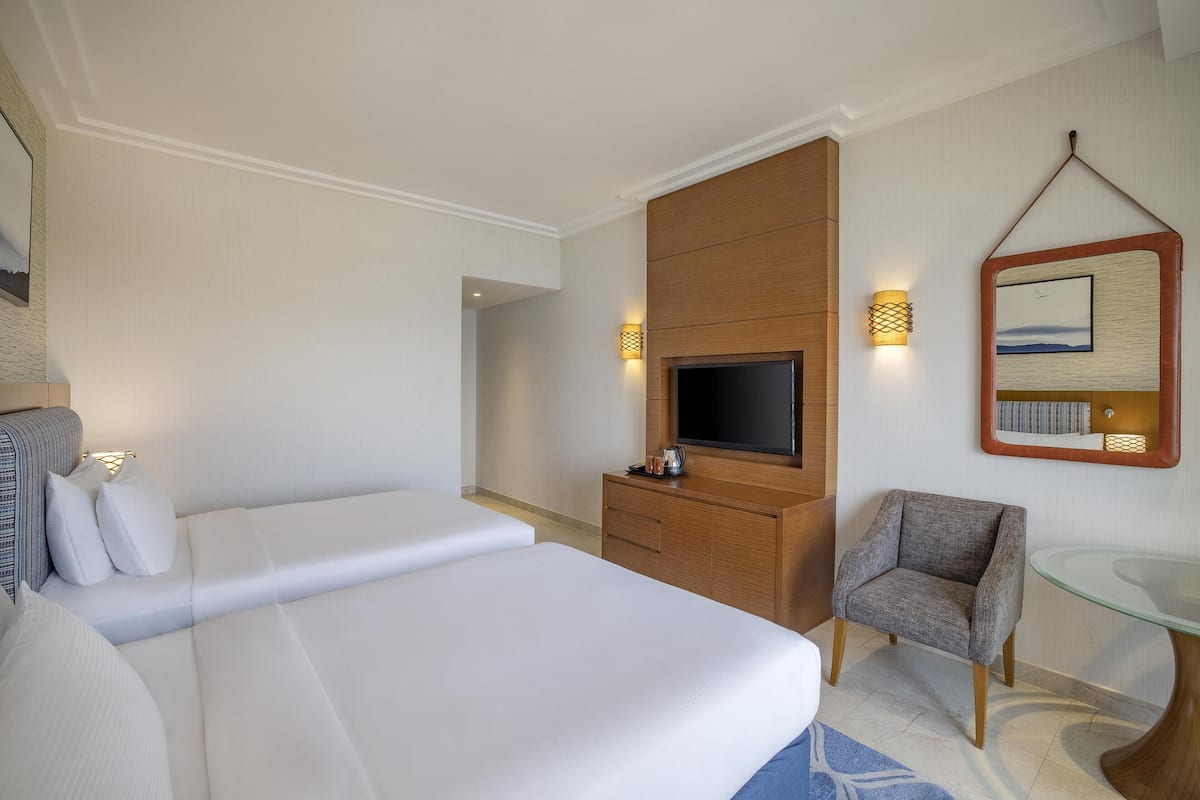 A hotel room with a bed, a TV, a chair, a glass table, and a wall-mounted mirror.