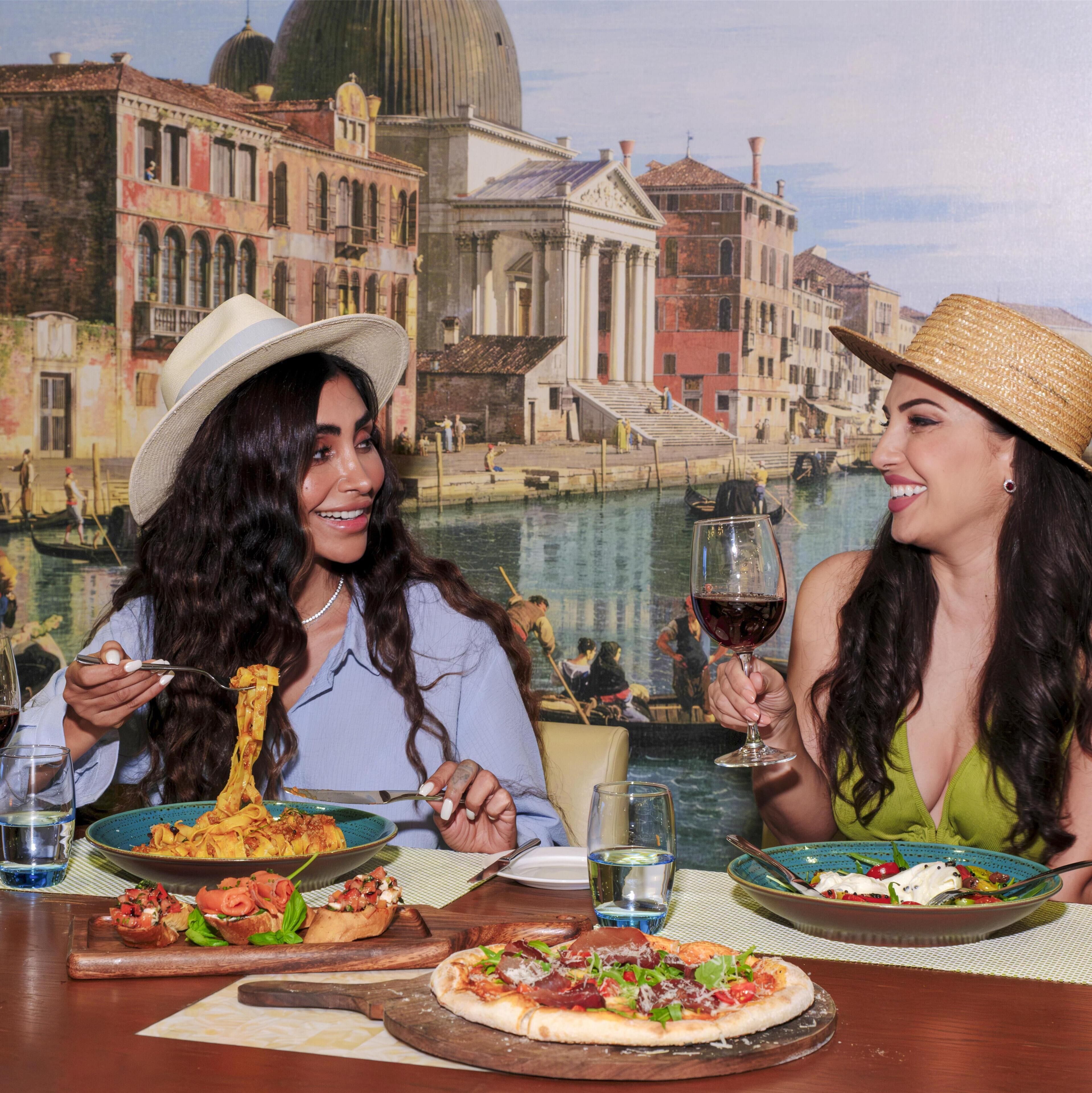 A dining table with plates of food, a pizza, and a glass of wine.