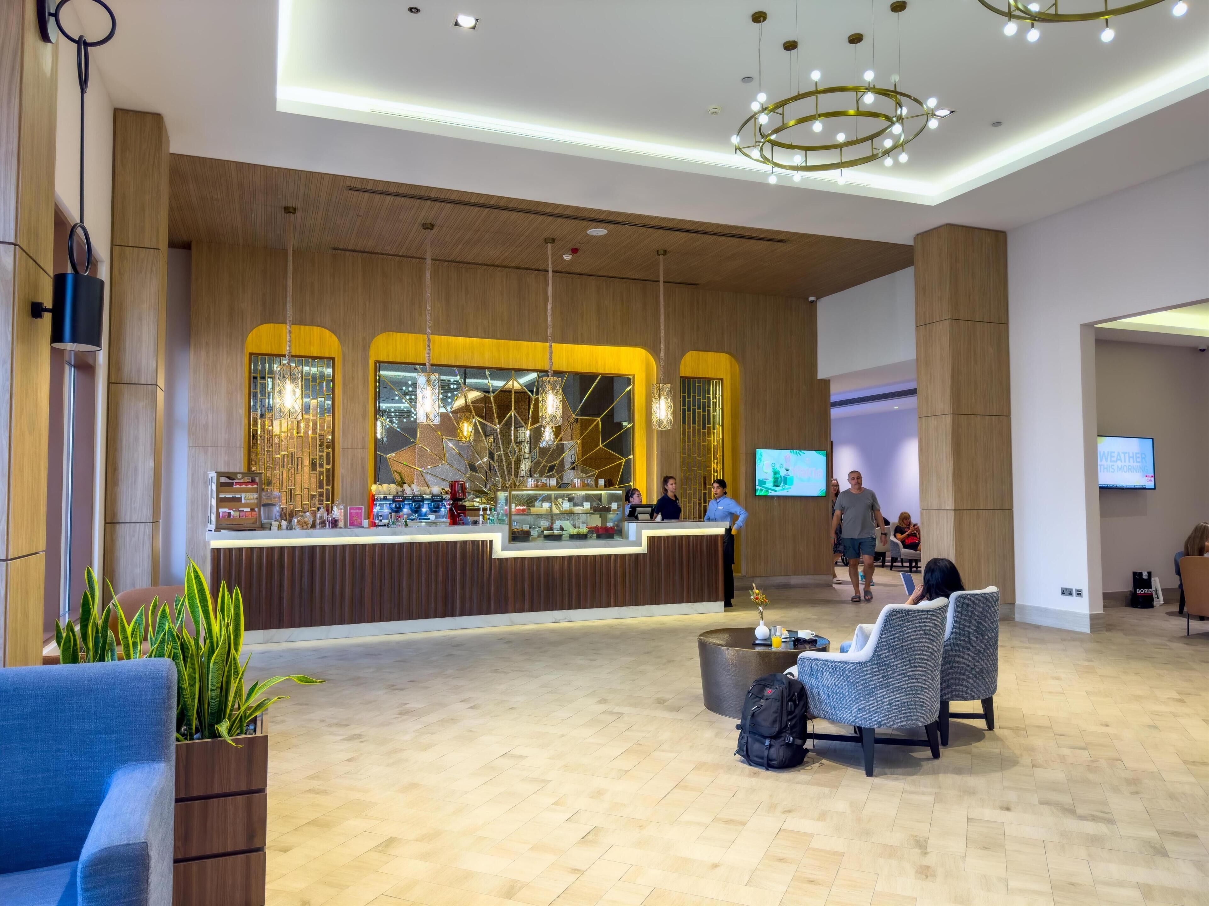 A hotel lobby with a reception desk, seating area, and a TV displaying the weather.