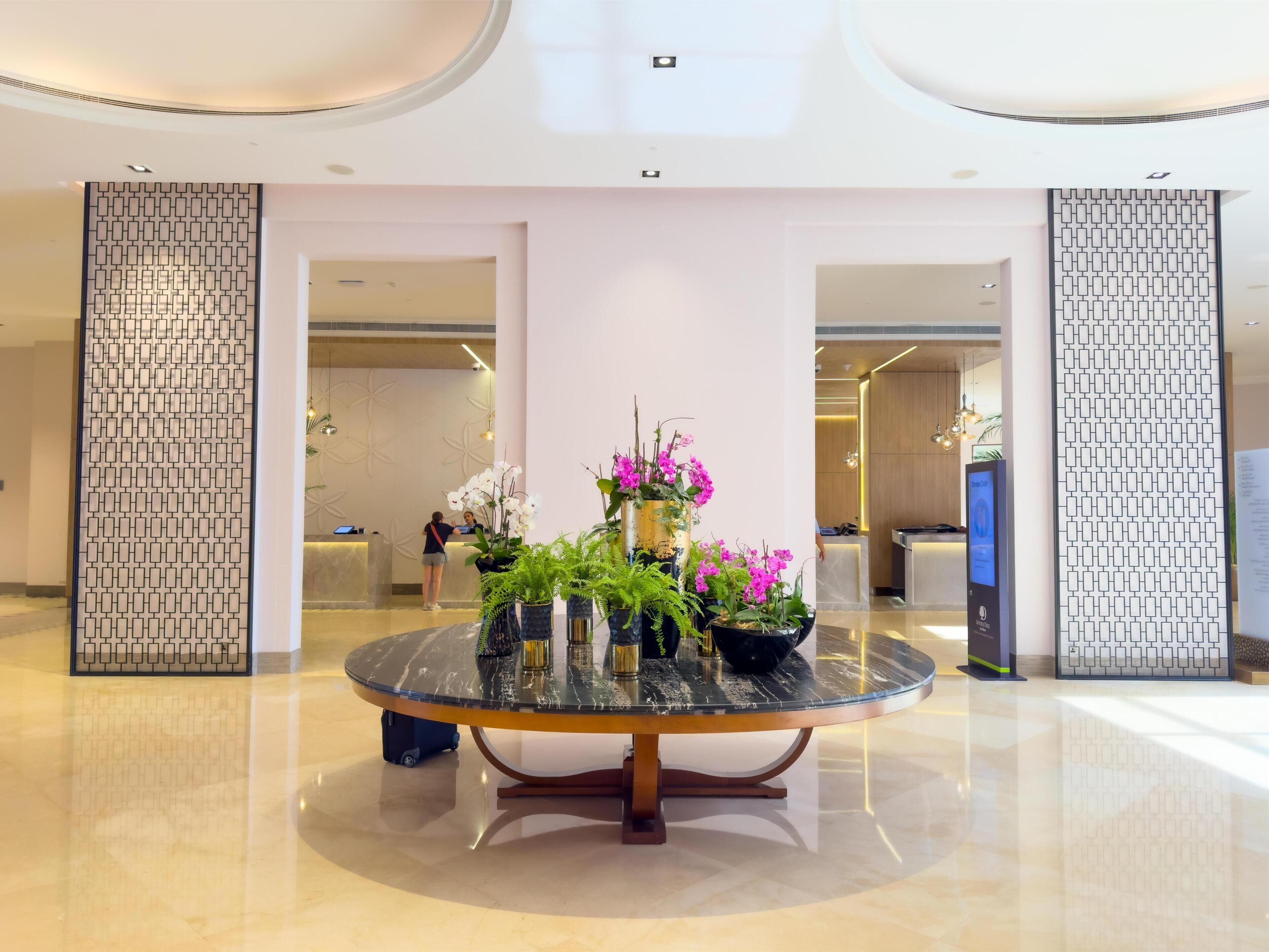 A lobby with a reception desk, a round glass table with plants, and a modern interior design.
