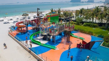 Un parque acuático con toboganes y piscinas, una playa y palmeras.