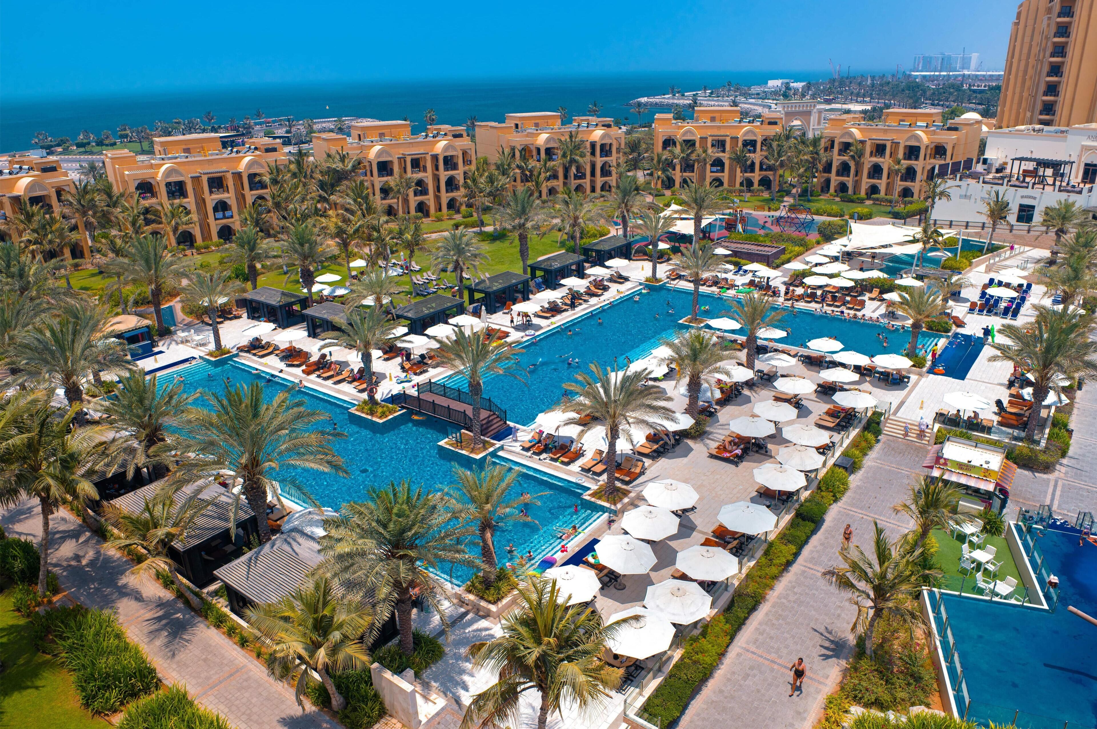 A resort with multiple swimming pools, palm trees, and a view of the ocean.
