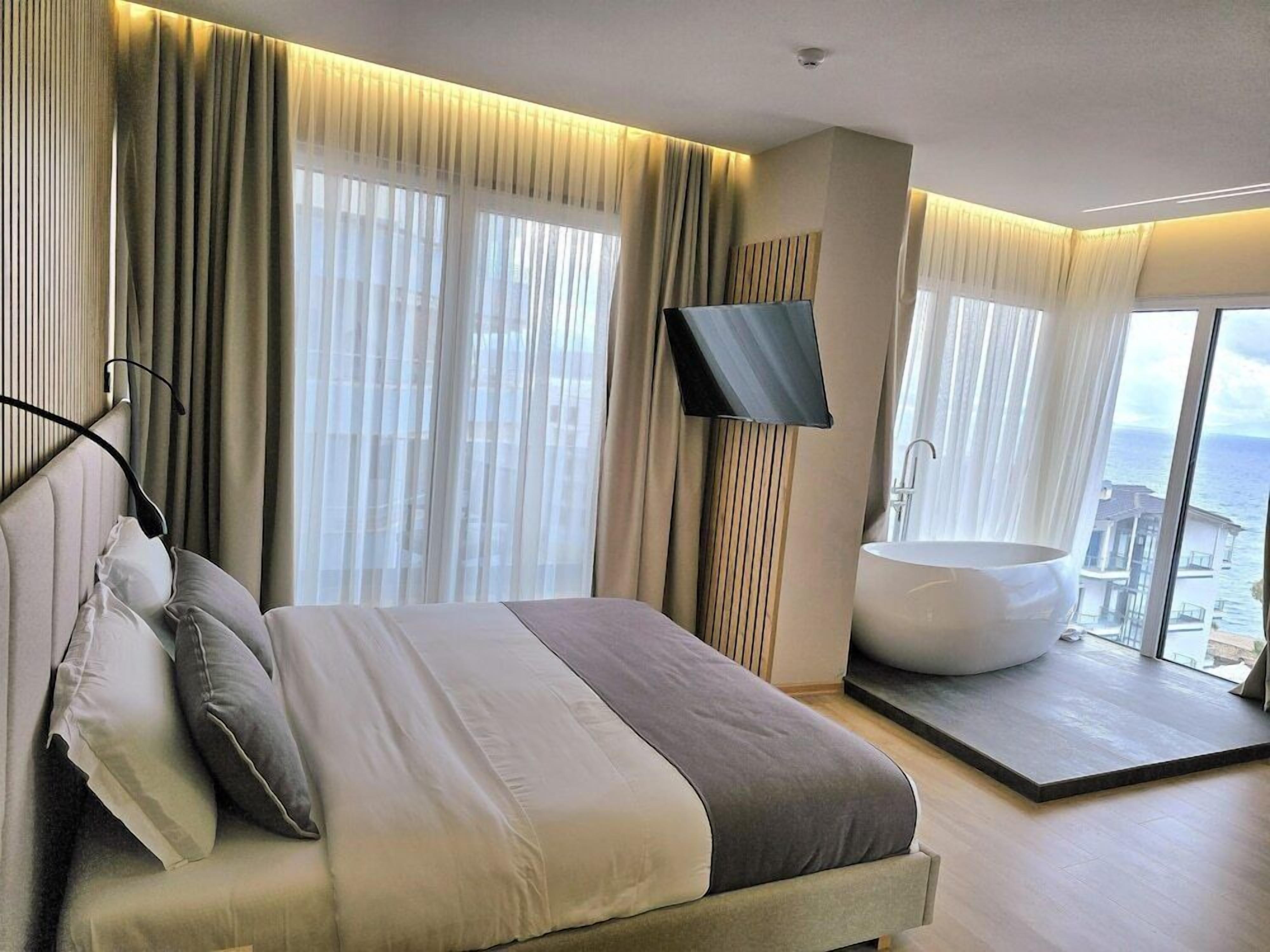 Habitación de hotel moderna con una cama grande, una bañera y vista al mar.