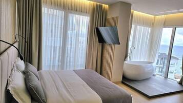 Habitación de hotel moderna con una cama grande, una bañera y vista al mar.