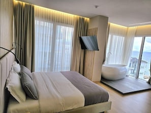 Quarto de hotel moderno com uma cama grande, uma banheira e vista para o mar.