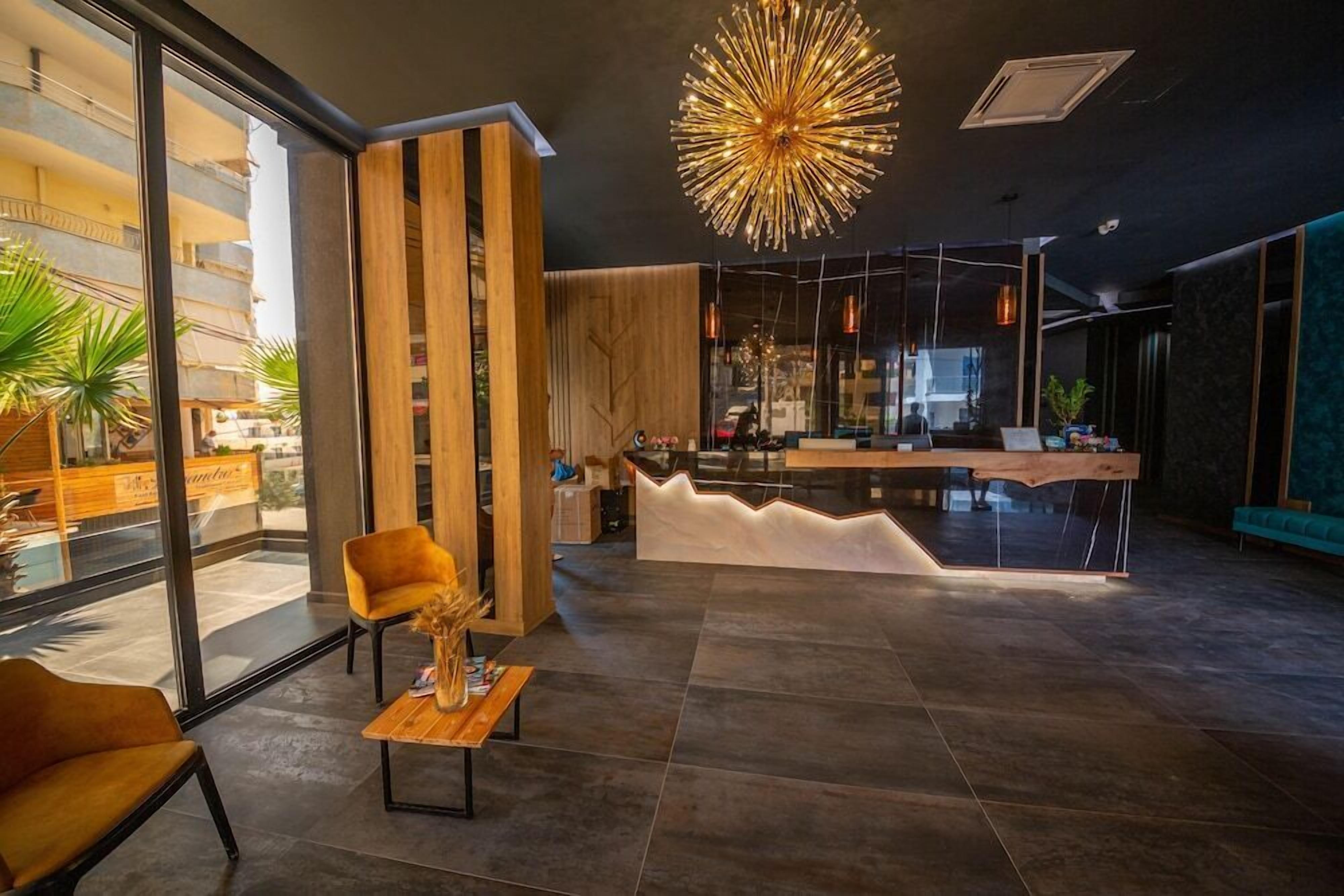 A modern reception area with a wooden reception desk, a large chandelier, and a seating area with a sofa and a table.