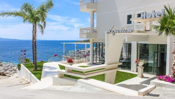 A hotel with a balcony overlooking the sea, a palm tree, and a sign that reads "Hotel Apollon." - Apollon Hotel (SARANDE)