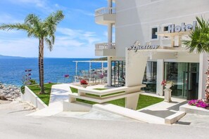 Un hôtel doté d’un balcon donnant sur la mer, d’un palmier et d’une enseigne indiquant « Hôtel Apollon ».