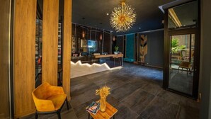 A modern interior with a reception desk, a yellow chair, a table with a vase, and a unique ceiling light. - Apollon Hotel (SARANDE)