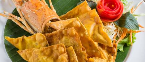 A plate of food with a lobster tail, fried items, and a rose-shaped vegetable on a banana leaf.