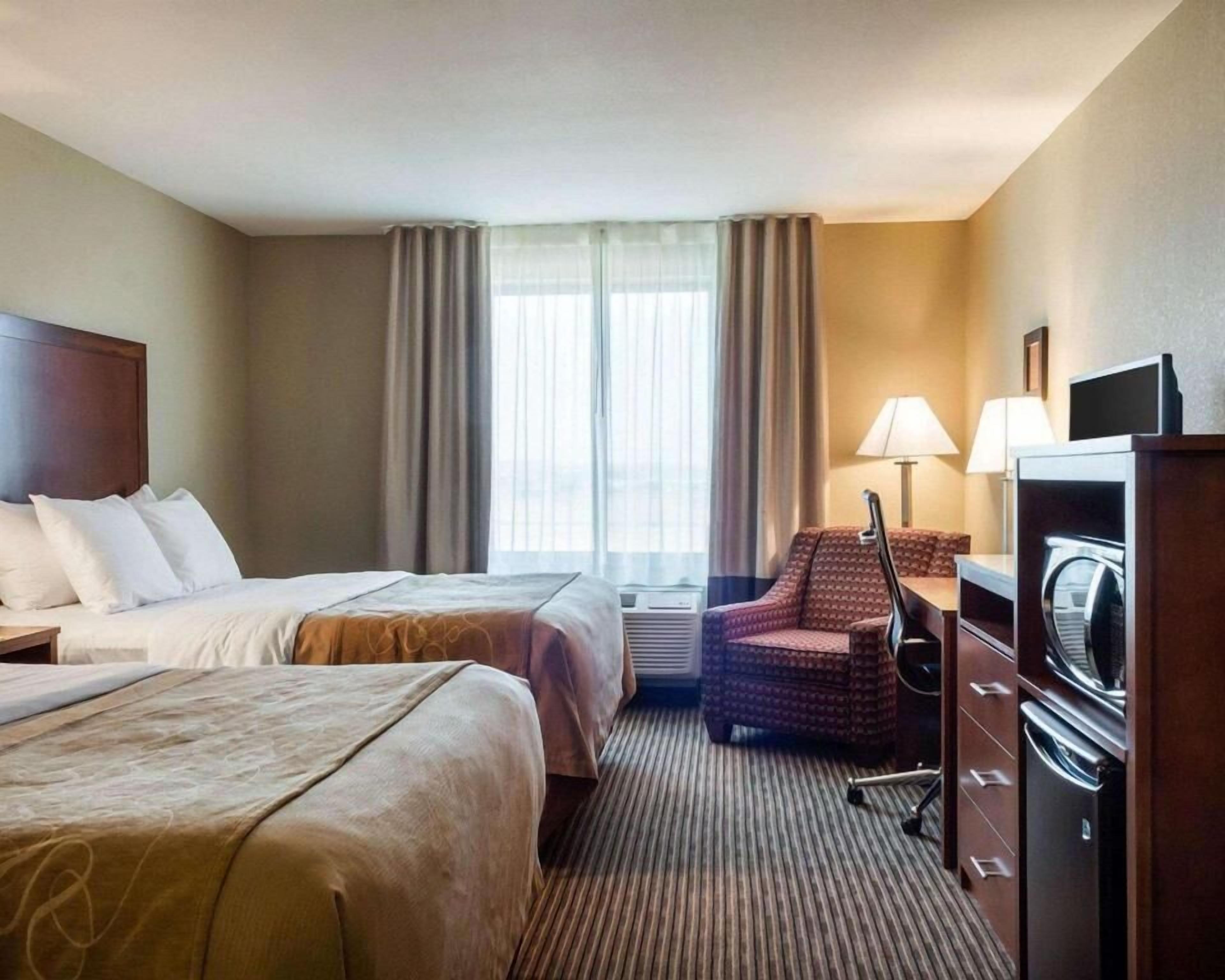 A hotel room with two beds, a desk with a chair, a TV, and a window with curtains.