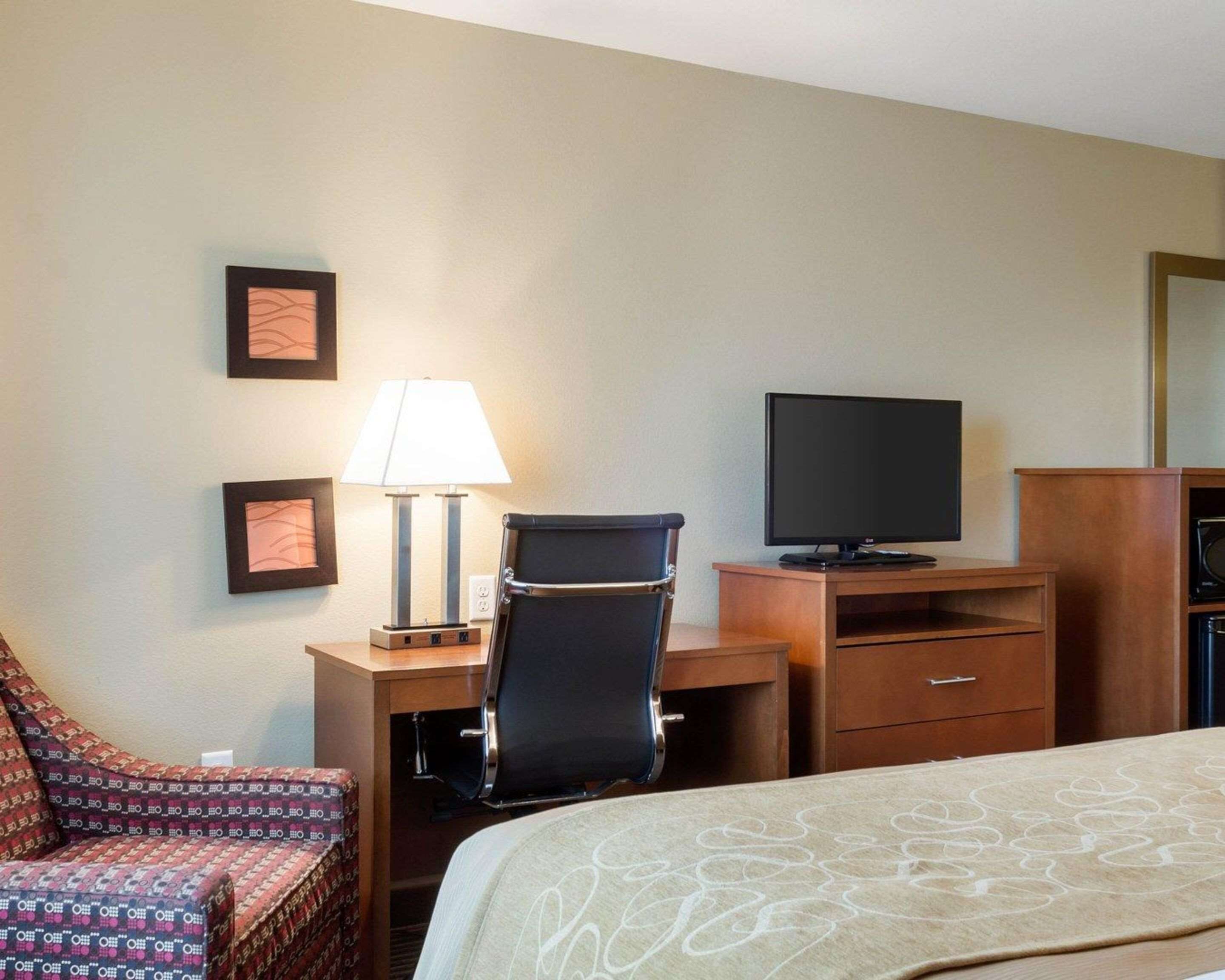 A hotel room with a bed, a desk with a computer and a lamp, a TV, and a chair.